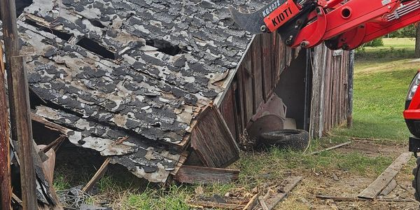 Dilapidated barn roof being removed by machinery.