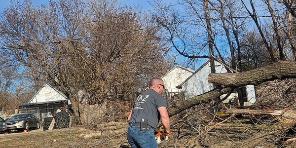 Man cutting fallen tree branches in a yard.