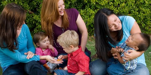 Moms smiling and holding watching their children play