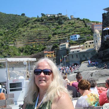 Tourists on a boat approaching a scenic coastal village with terraced hills and historic buildings.