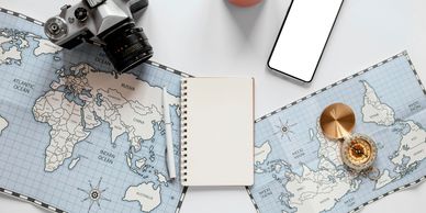 Travel essentials including a camera, map, compass, smartphone, notebook, and coffee cup.