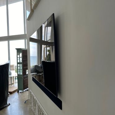 Wall-mounted TV reflecting a bright room with large windows and ocean view.