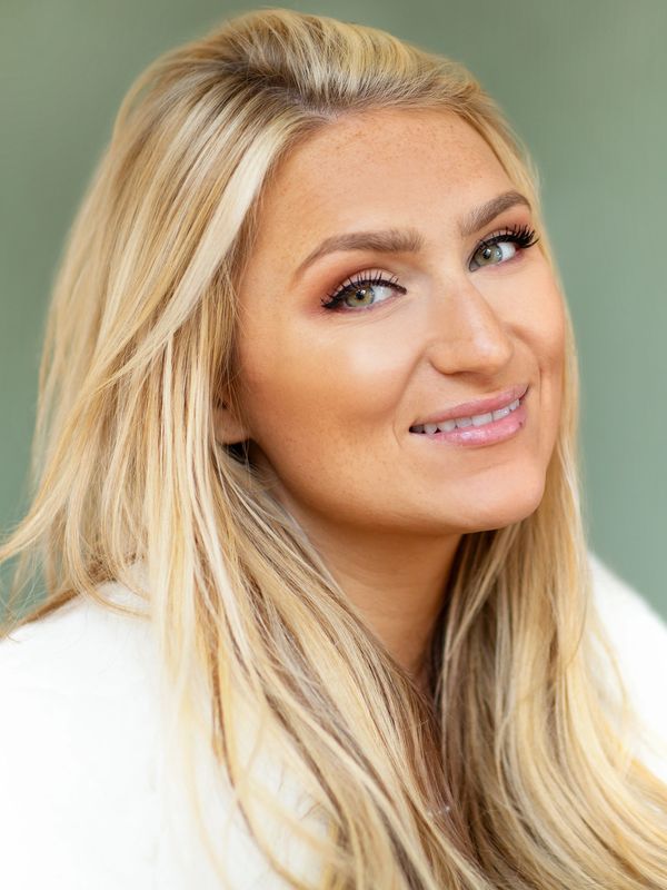 Close-up portrait of a smiling blonde woman with green eyes and natural makeup.