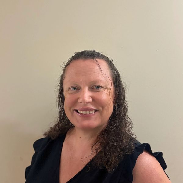 Smiling woman with curly hair in a black top against a plain wall.