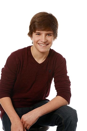 Smiling teenage boy sitting on a stool against a white background.