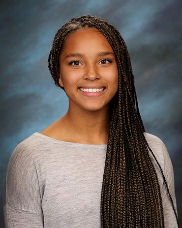 Young woman with long braided hair smiling against a blue-gray background.