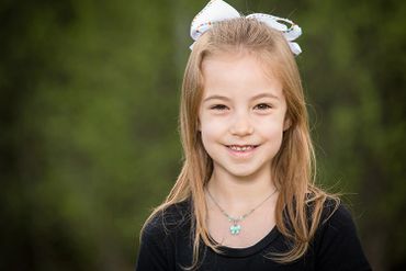 Smiling young girl with a white bow and butterfly necklace.