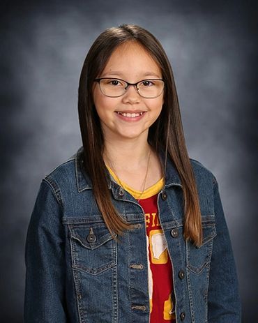 Young girl with glasses smiling in a denim jacket.