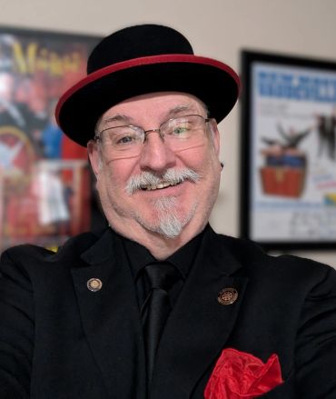 Smiling man wearing a black hat with a red trim and matching suit.