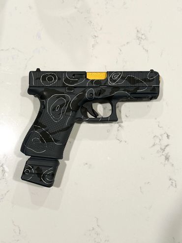 Custom black handgun with white abstract patterns and a gold slide section.