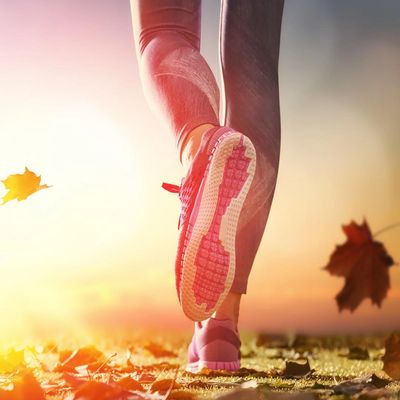 Close-up of a person jogging on a leaf-covered path during sunset.