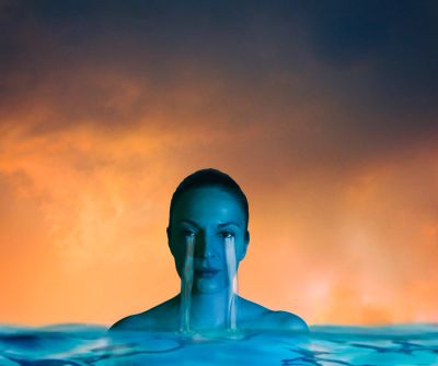 Surreal image of a woman with tears flowing like waterfalls into water.