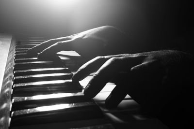 Hands playing piano keys in dramatic black and white lighting.