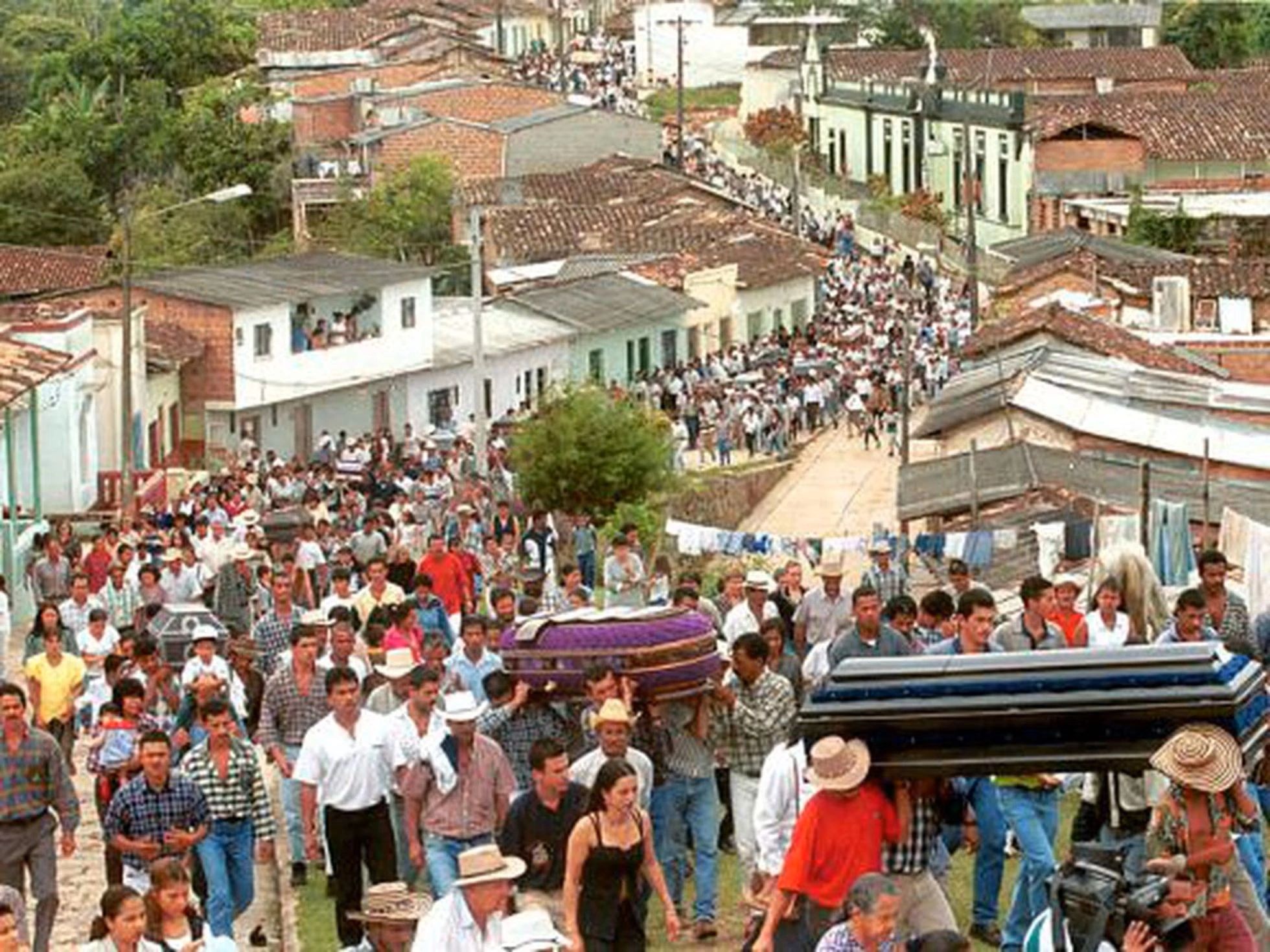 Large crowd participates in a funeral procession in a small town.