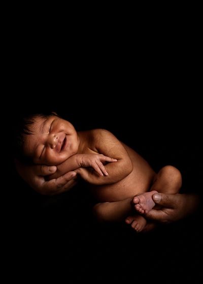 A newborn baby peacefully sleeping in adult hands against a black background.