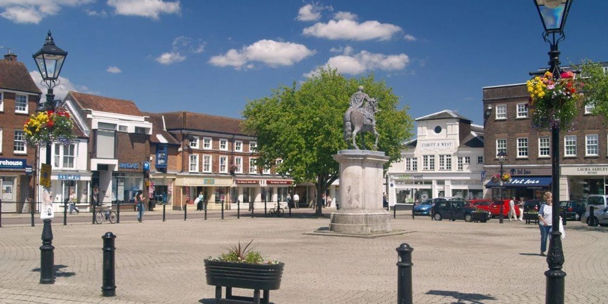 Historic town square with statue and hanging flower baskets.