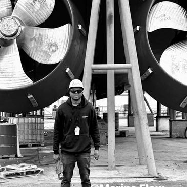Man in sunglasses and hoodie standing in front of industrial fans in a black and white photo.