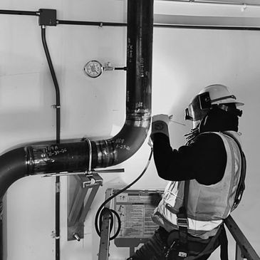 A worker in safety gear inspects a large industrial pipe indoors.