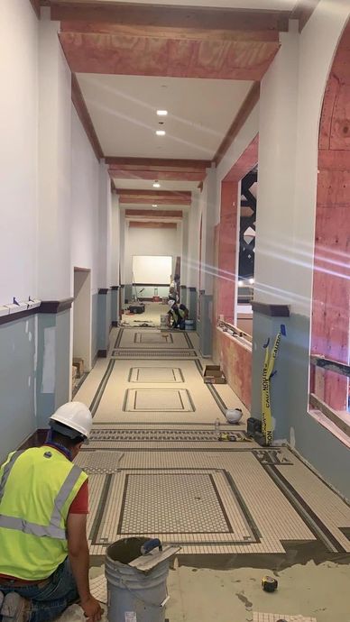 Workers installing decorative floor tiles in a corridor.