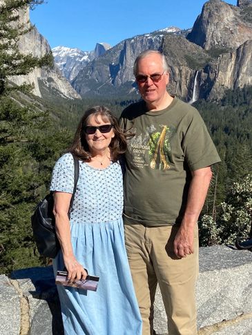 A couple poses with a mountainous landscape and waterfall behind them.