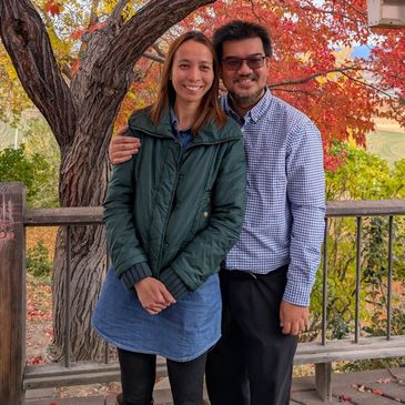 Couple smiling outdoors with autumn leaves in the background.