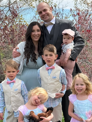 A happy family dressed in formal attire posing outdoors among blossoming trees.