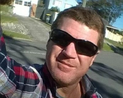 Man wearing sunglasses and a plaid shirt taking a selfie outdoors.