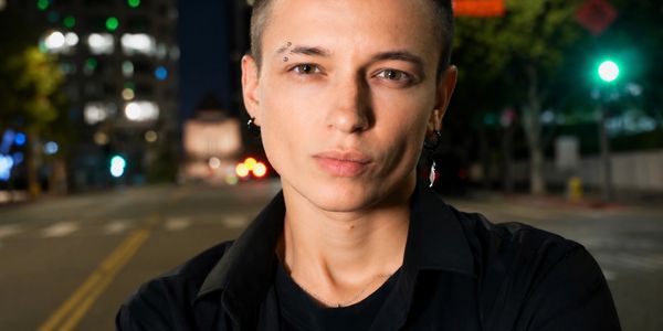 Person with earrings and eyebrow piercing standing on a city street at night.