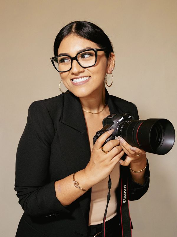 Smiling woman with glasses holding a Canon camera.