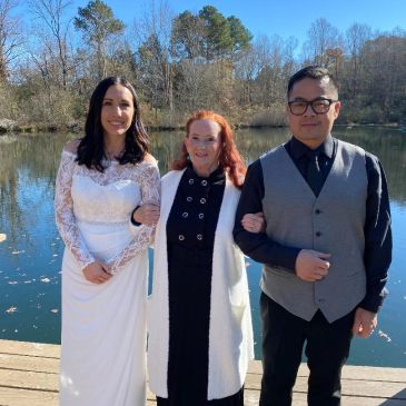 Three people posing by a lake on a sunny day.