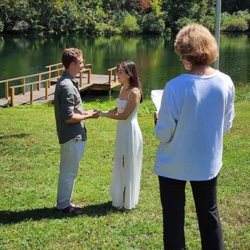Couple holding hands near a lake during a ceremony.