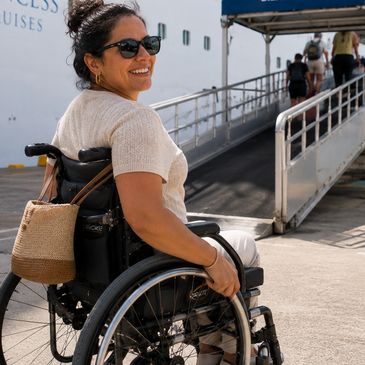Smiling woman in a wheelchair near a cruise ship ramp.