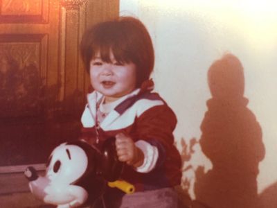 A toddler riding a Mickey Mouse toy with a shadow on the wall.