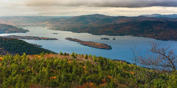 Scenic view of a lake surrounded by forested hills under a cloudy sky.
