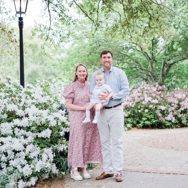 A smiling family of three posing outdoors among blooming flowers.
