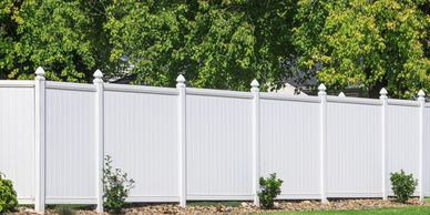 White vinyl privacy fence with greenery and trees behind it.