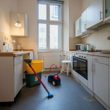 A kitchen with cleaning tools including a mop, buckets, and a vacuum cleaner on the floor.