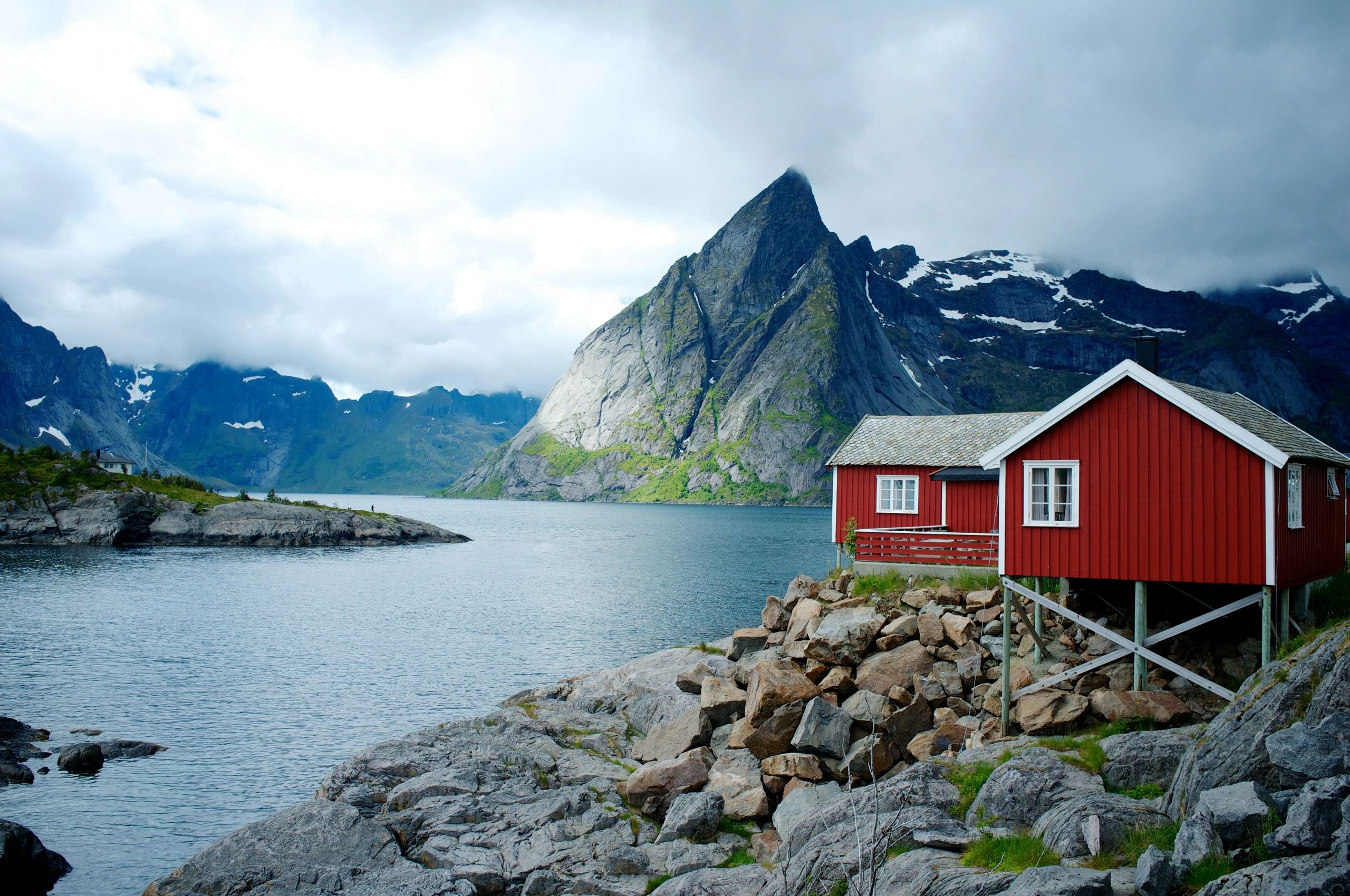 Red cabins on rocky shore with towering mountain backdrop.