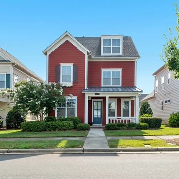A charming red two-story house with a blue door and lush green landscaping.