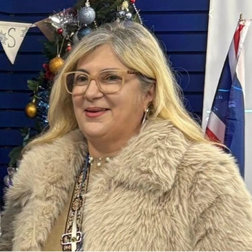 Woman with glasses in a beige fur coat smiling indoors.