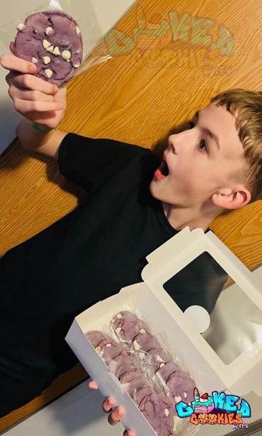 Boy excitedly holding a purple cookie from a box of cookies.