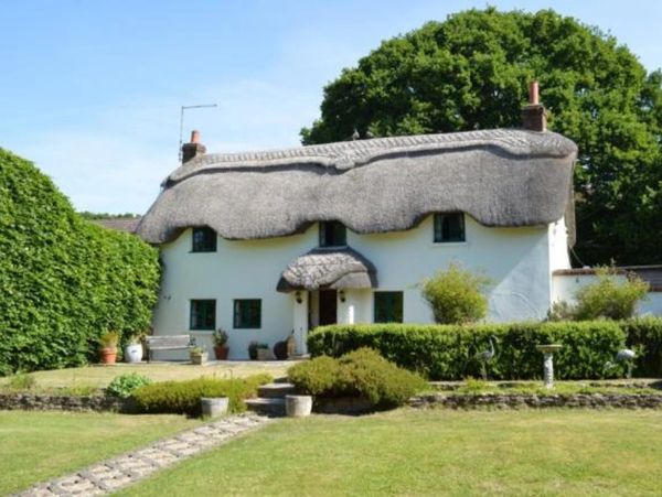 Quaint white cottage with a unique thatched roof and lush garden surroundings.