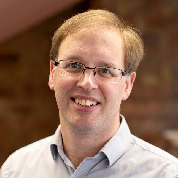 Smiling man with glasses and light brown hair in a casual shirt.