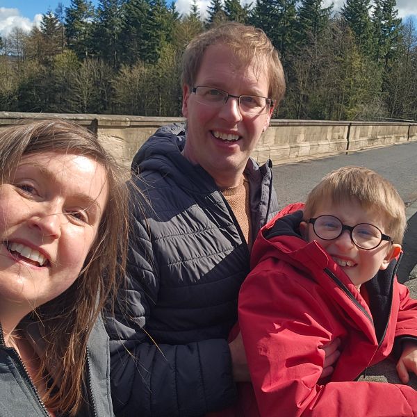 A happy family of three outdoors, smiling at the camera.