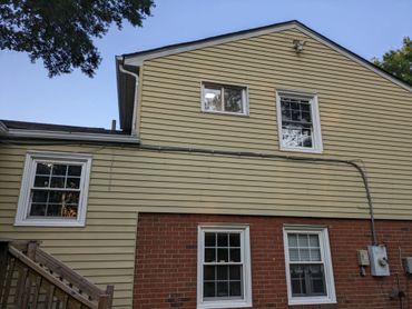 Side view of a house with yellow siding and brick lower wall.