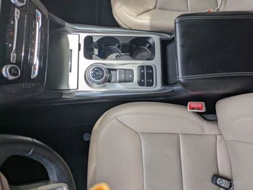 Car interior showing center console with gear dial and beige seats.