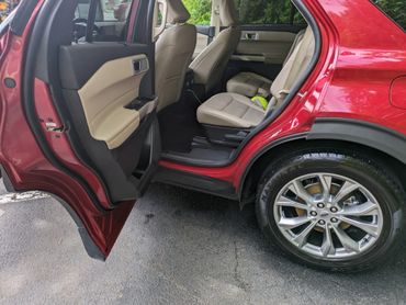 Open rear door of a red SUV showing beige leather seats and alloy wheels.