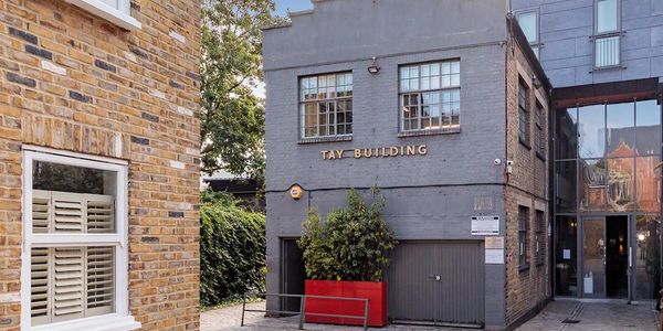 The Tay Building with a gray facade and red planter in a cobblestone courtyard.