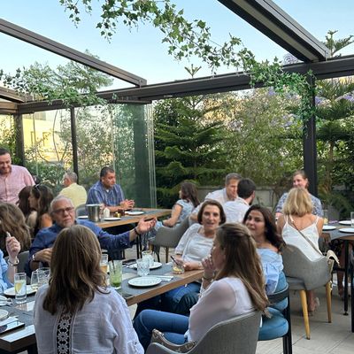 People enjoying a meal together in a glass-enclosed patio with greenery.
