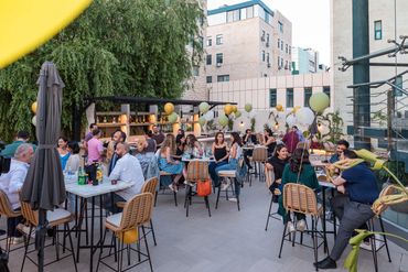 People socializing at an outdoor rooftop party with balloons and drinks.